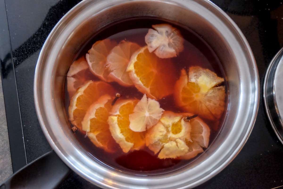 citrus slices boiling in red kinderpunsch in silver pot on stovetop.