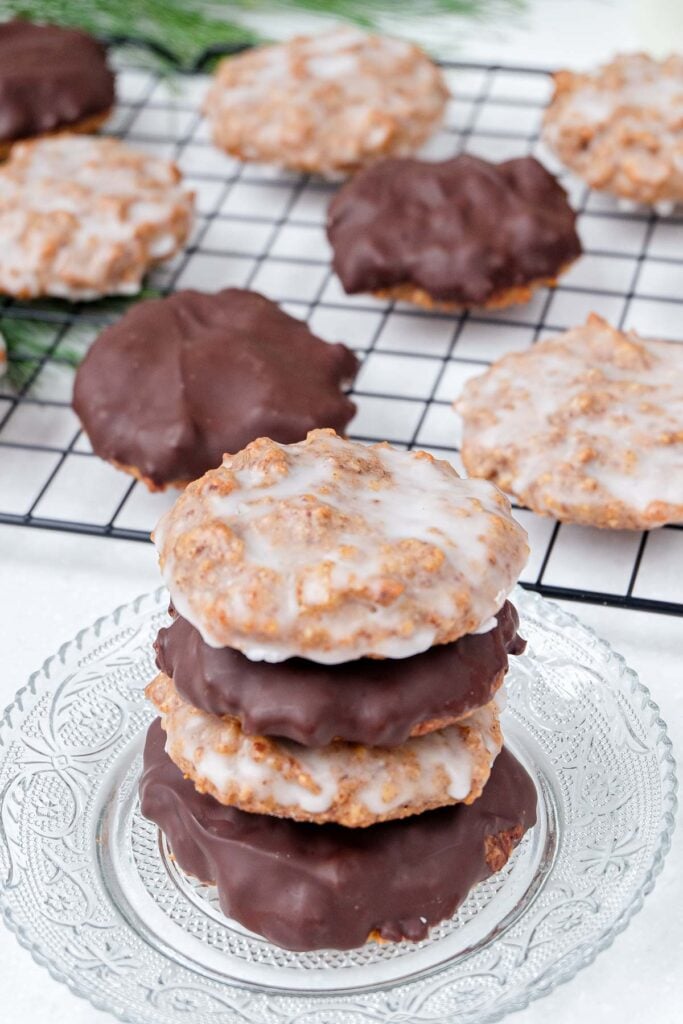 german gingerbread cookies stacked on plate with cookies on rack behind.