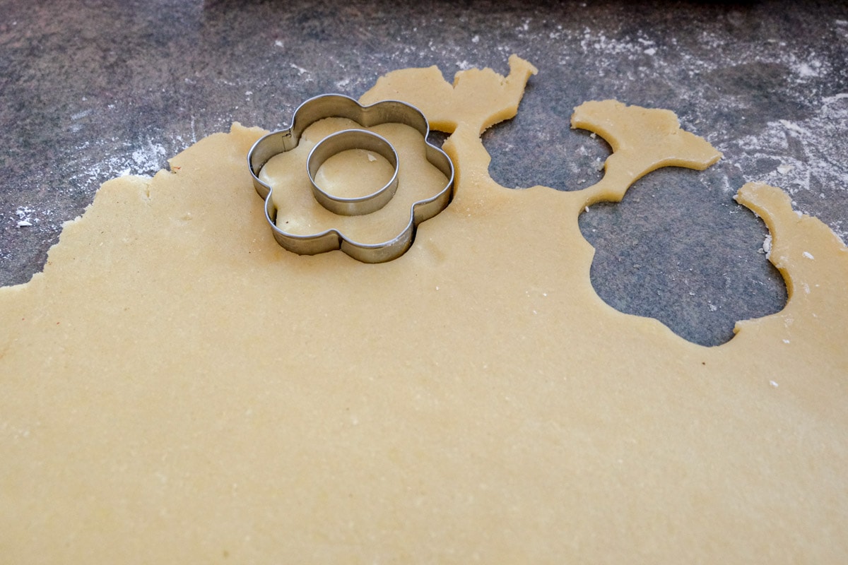 flower cookie cutter cutting through cookie dough on counter top.