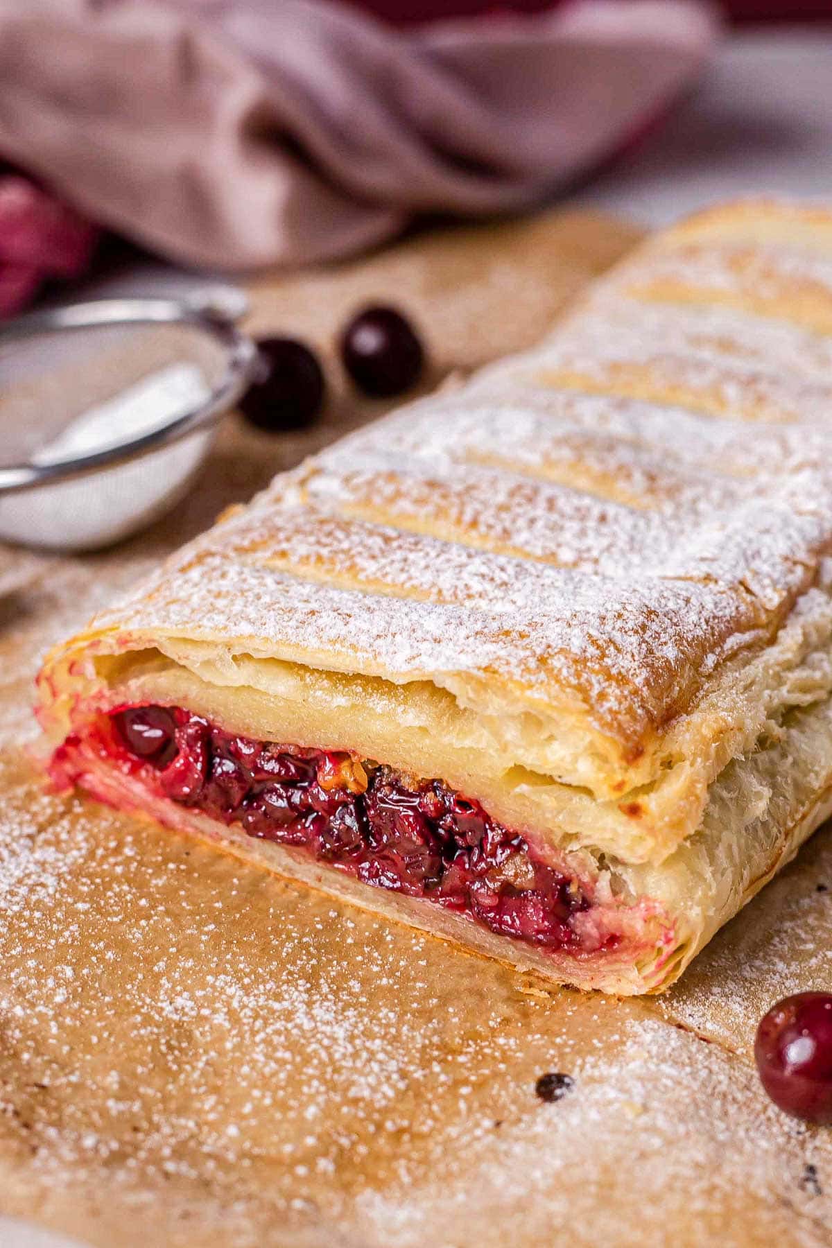 cherry strudel on parchment paper with end cut off showing cherry filling.