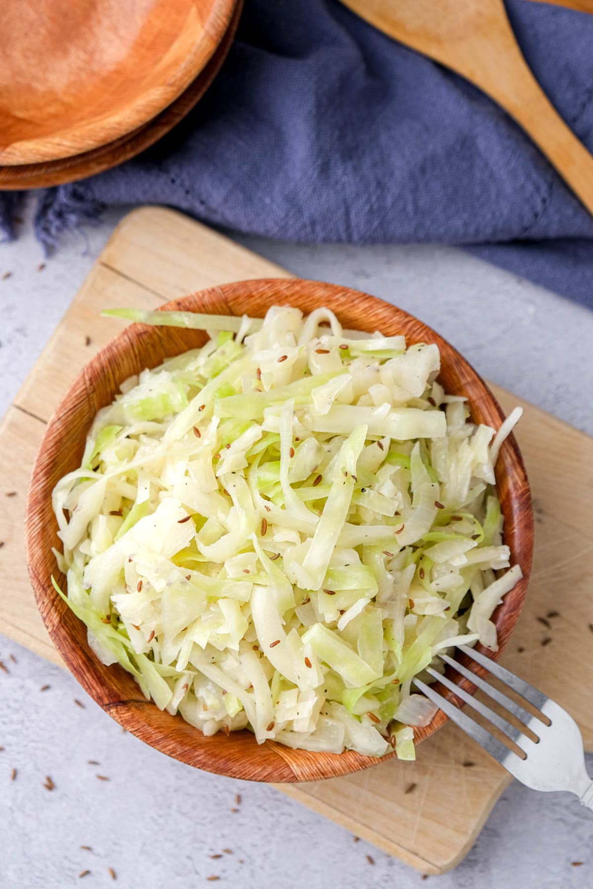 bowl of german coleslaw sitting on wooden board with silver fork beside.