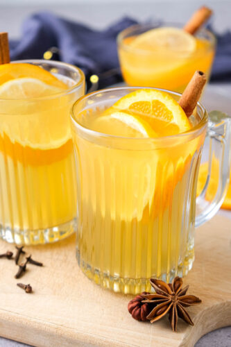 clear mugs of mulled white wine with citrus slices and cinnamon in each glass.