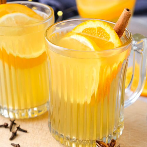 clear mugs of mulled white wine with citrus slices and cinnamon in each glass.
