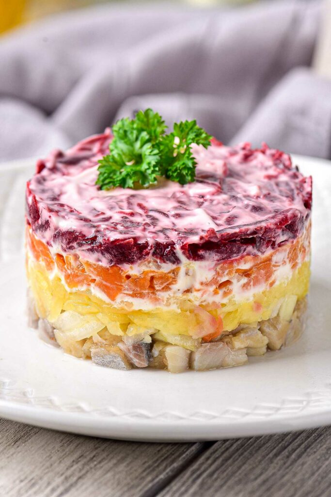 colorful layered herring salad on white plate with cloth behind.