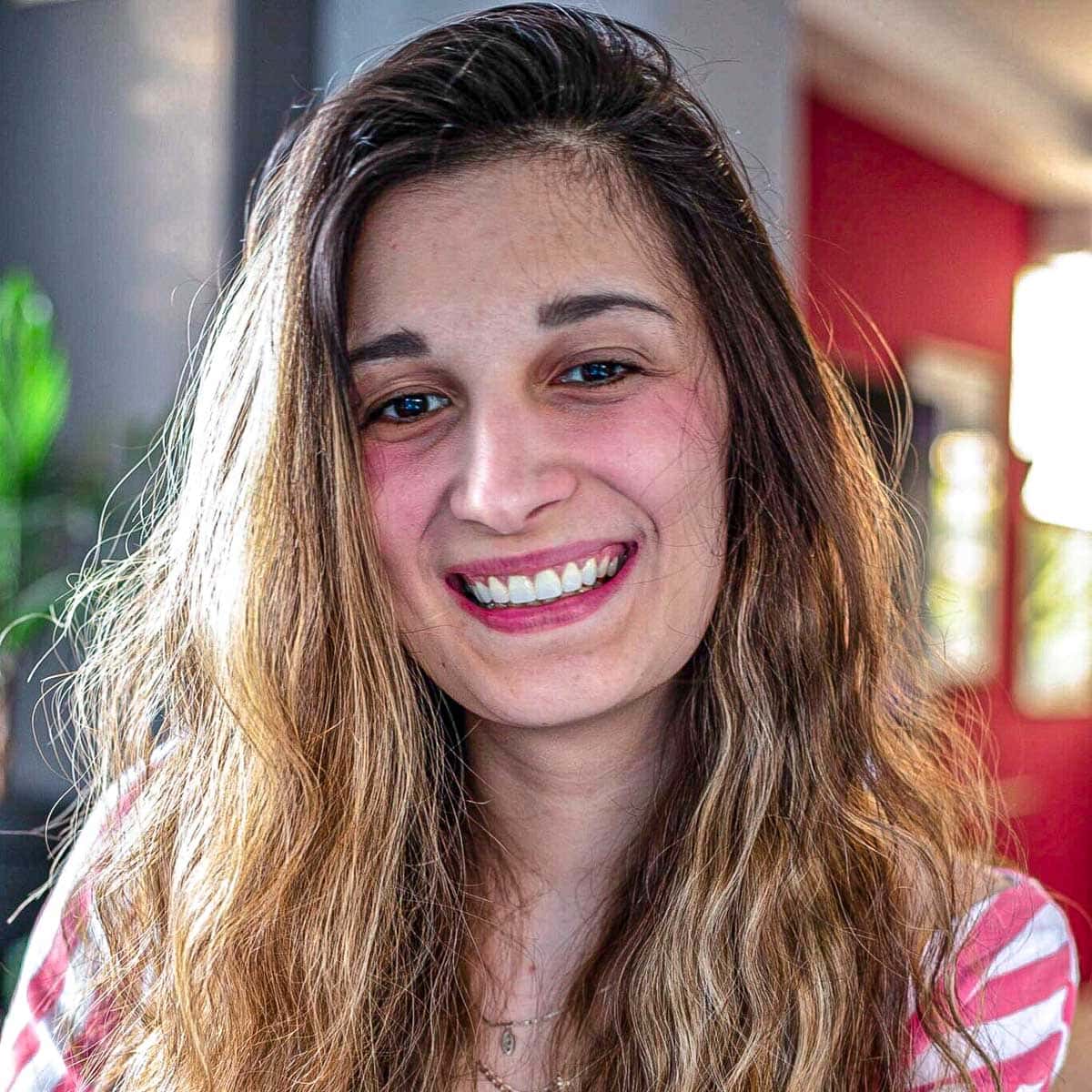 smiling woman with long brown hair and red walls behind.