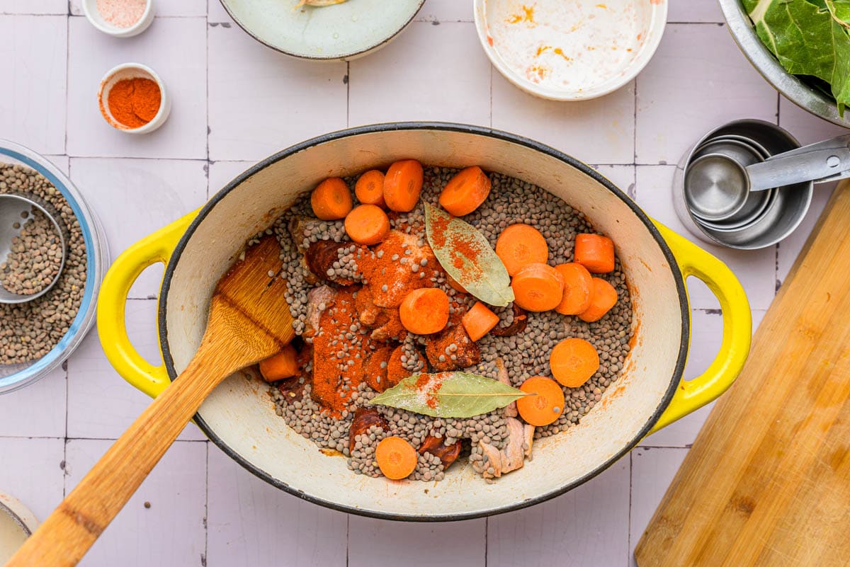 raw chopped carrots in large pot with lentils and wooden spatula stirring them around.