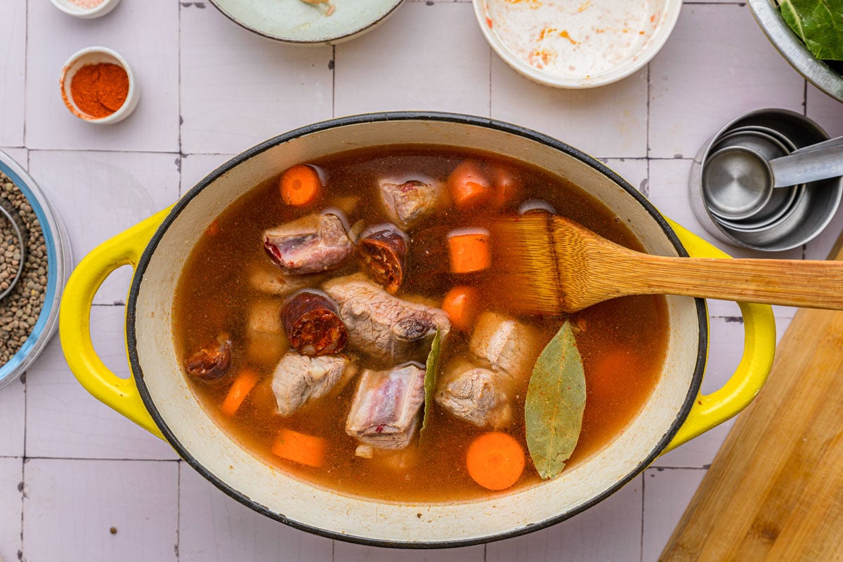 large pot filled with broth and pork ribs and chopped carrots.