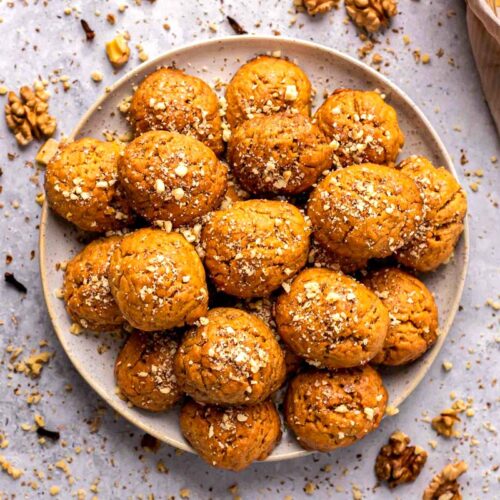 greek honey cookies in round plate with crumbled nuts around.