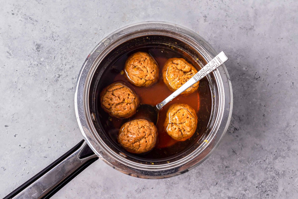 five greek honey cookies in silver pot of syrup sitting on counter.