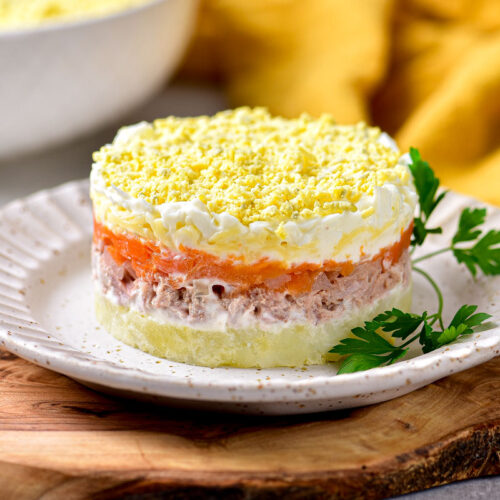 white plate with layer mimosa salad on it with parsley beside.