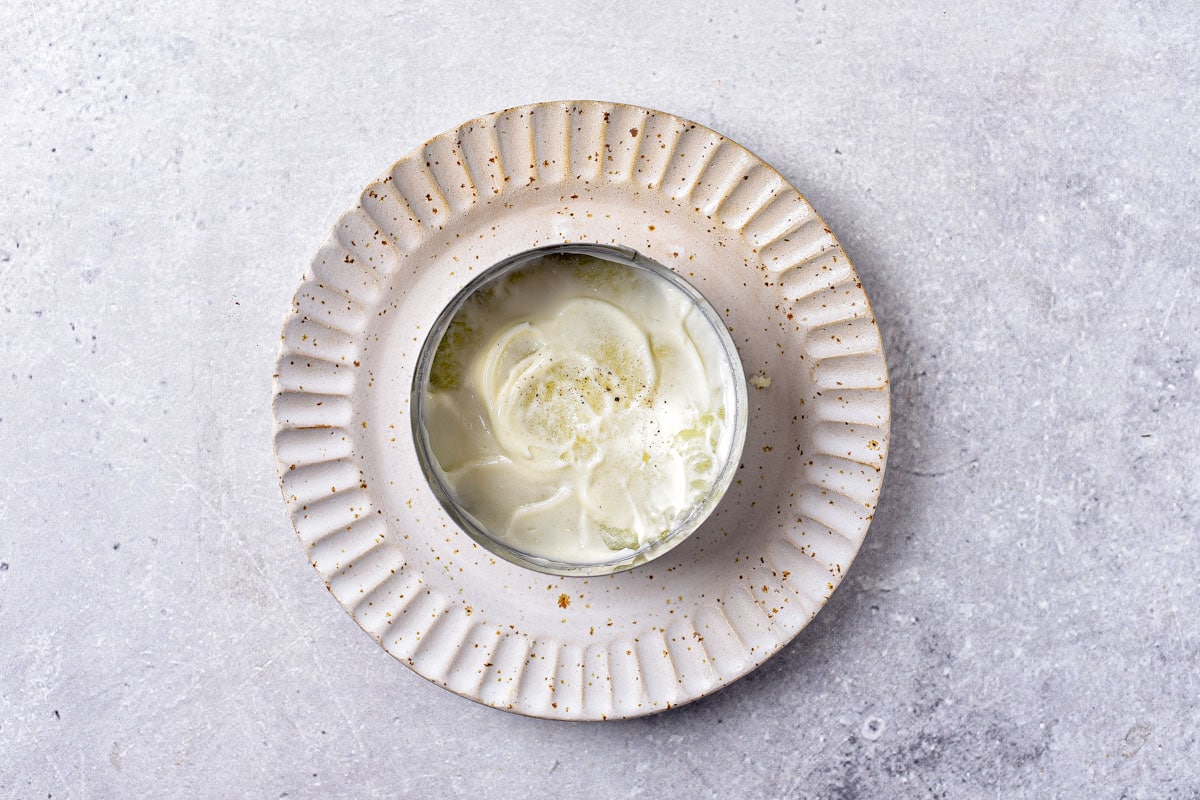 round metal form on plate with potatoes and mayo layered in the bottom.