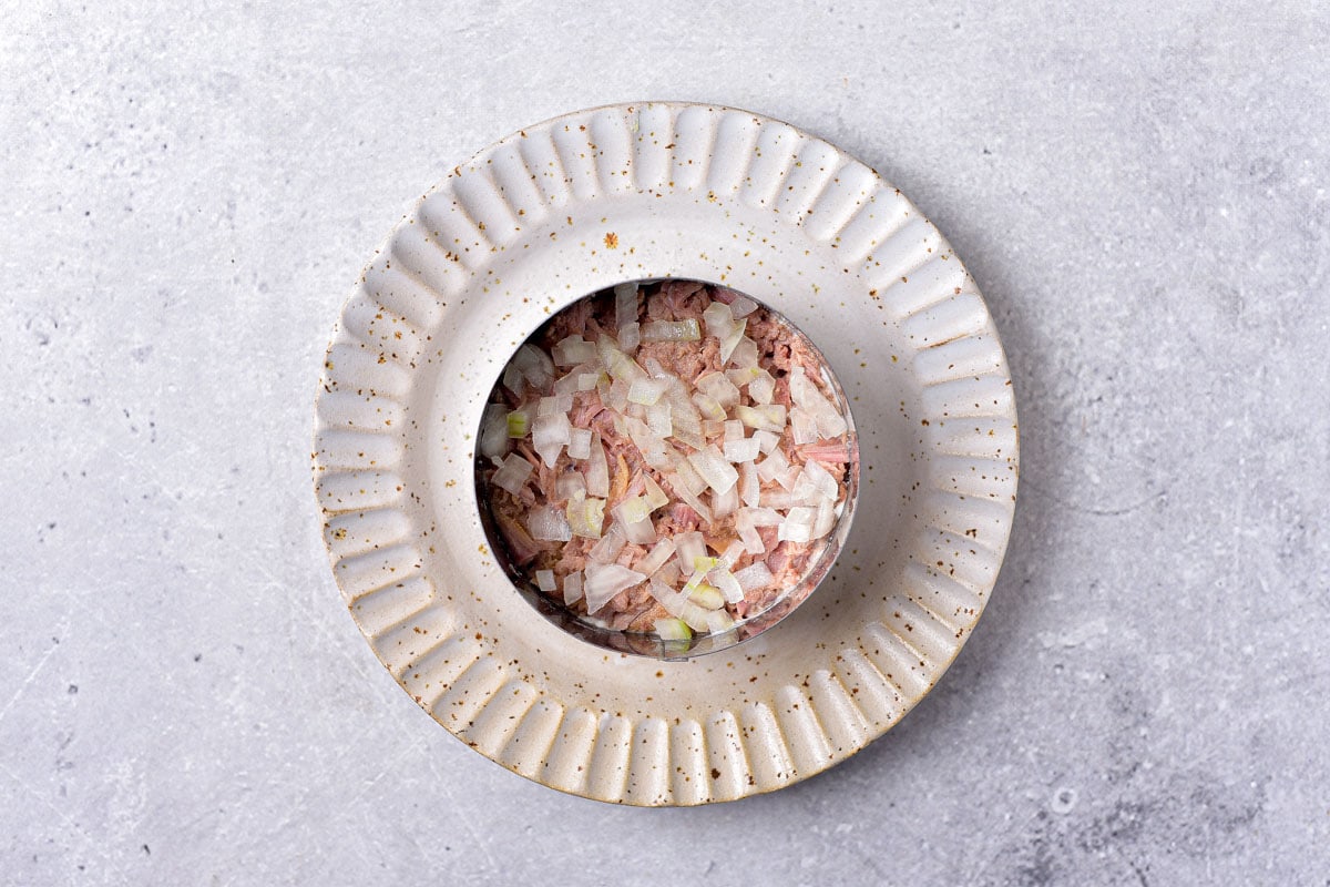 layers of tuna and onions in round metal form on white plate.