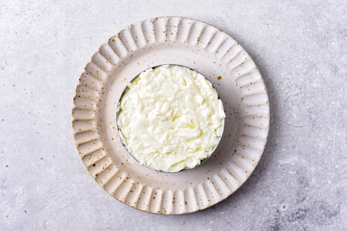 layer of egg whites and mayo spread into round metal form sitting on plate.
