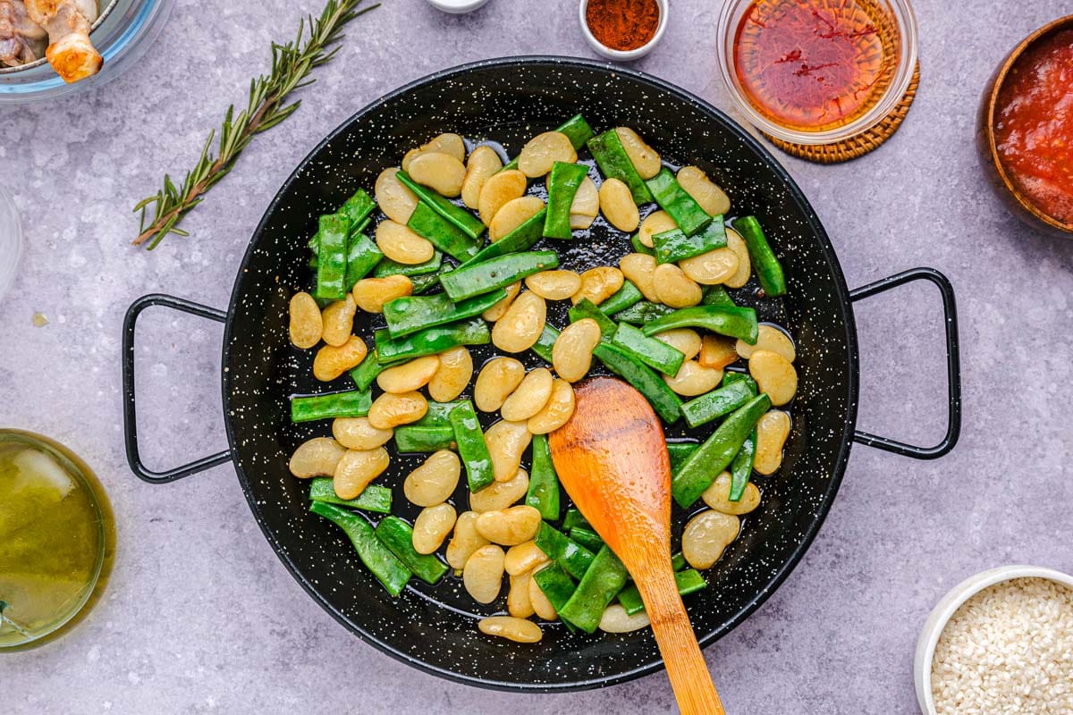white lima beans and pieces of green beans frying in large black pan.