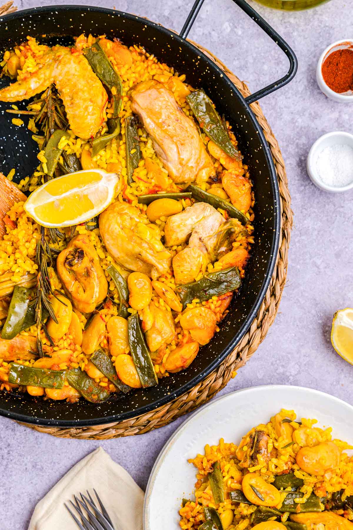 large black pan of paella with smaller white plate with a portion beside.