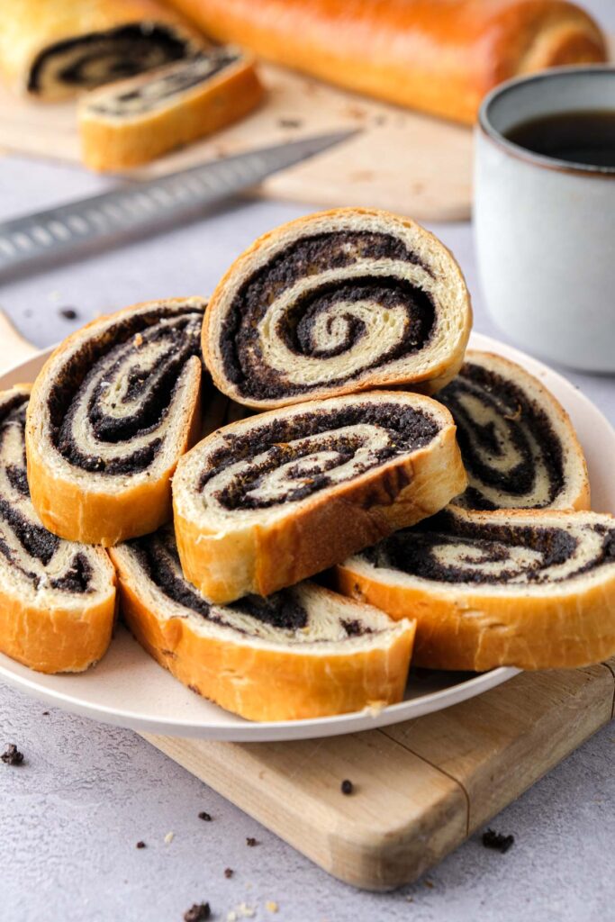 slices of poppy seed roll on plate with knife and other rolls behind.