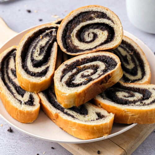 slices of poppy seed roll on white plate sitting on cutting board.