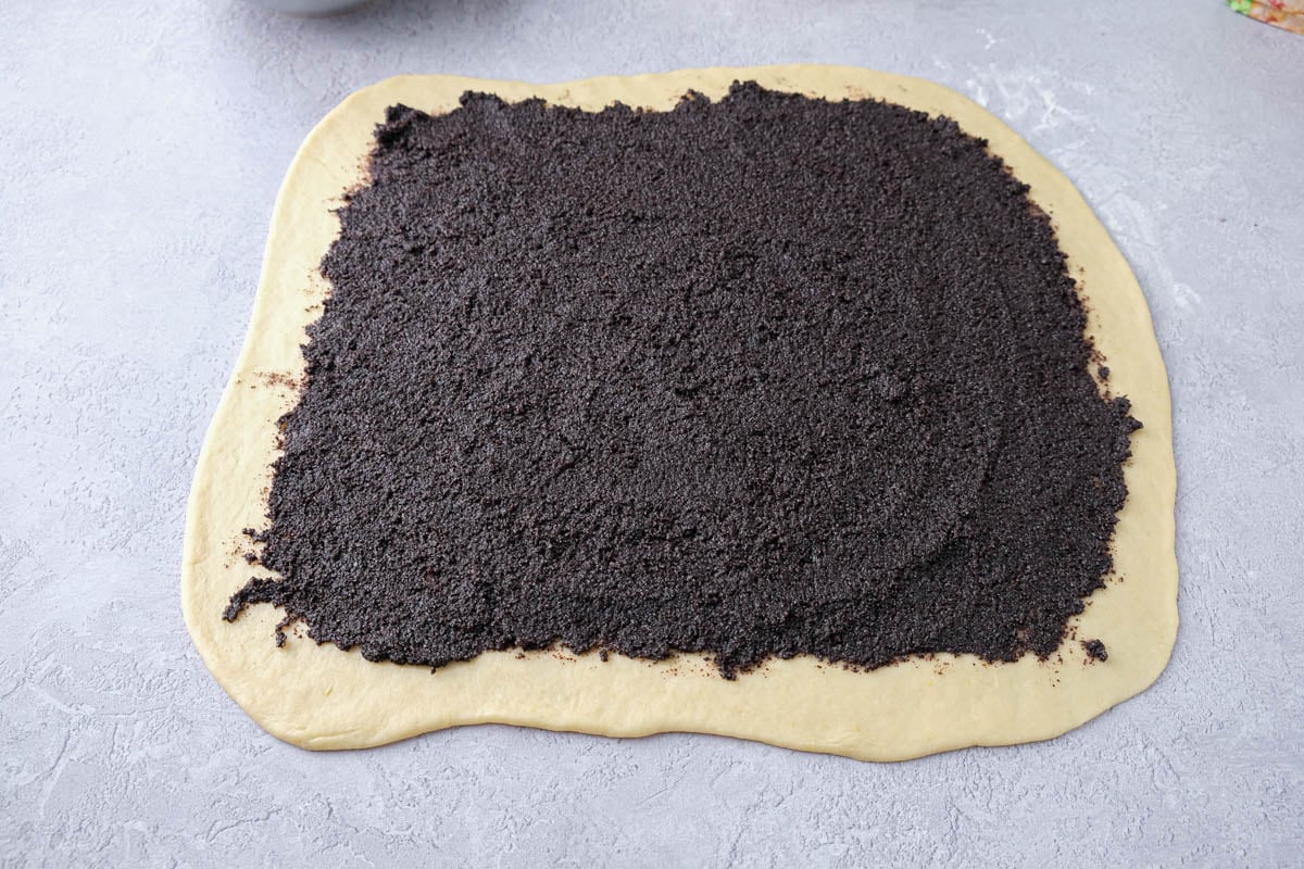 piece of dough with poppy seed filling spread out on it sitting on counter.
