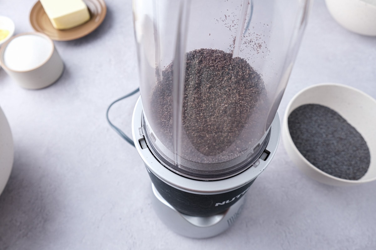 blender grinding poppy seeds with small bowl of seeds beside on counter.