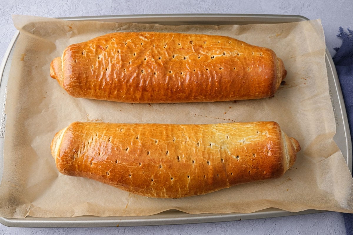 two golden brown baked poppy seed rolls on parchment paper tray.