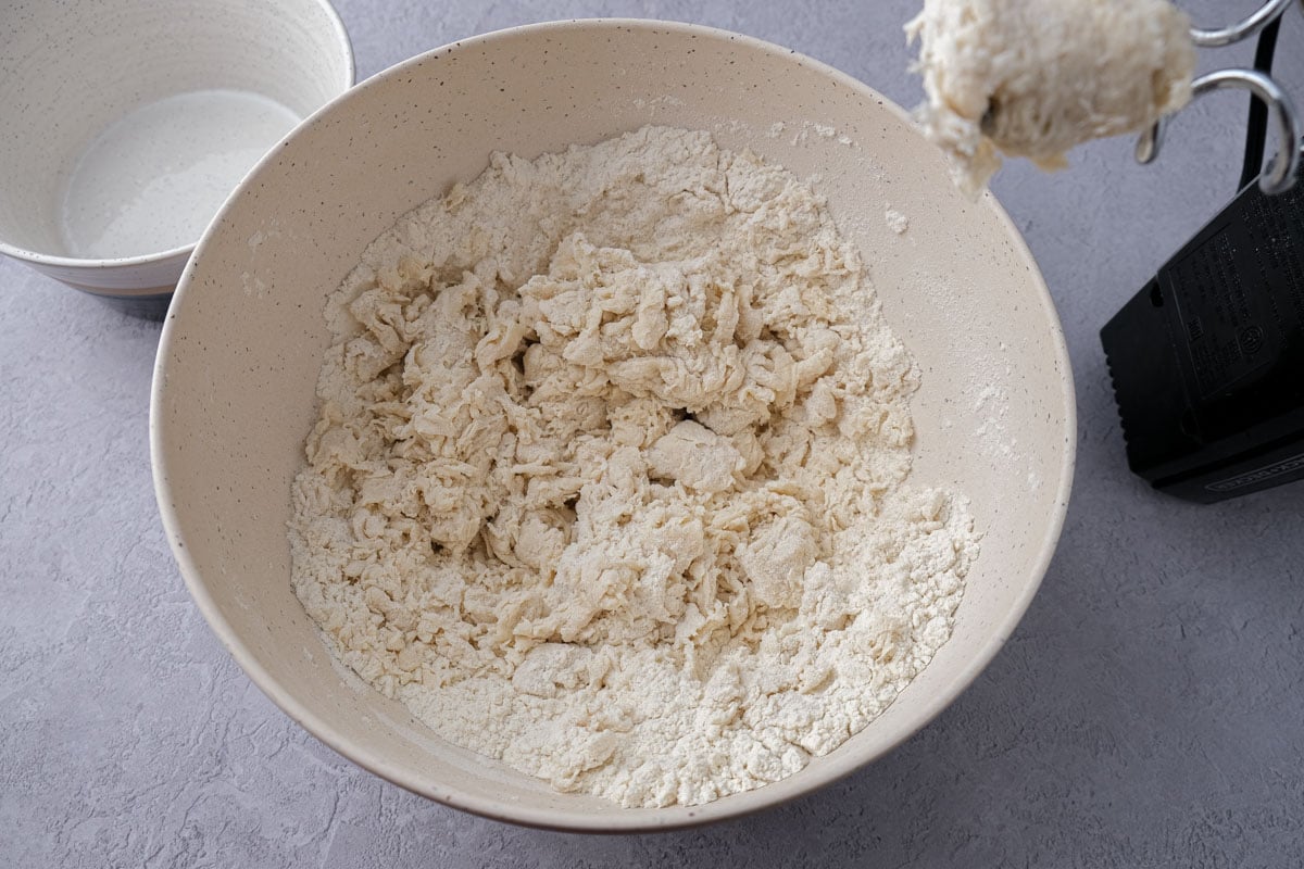 slightly wet dough ingredients in mixing bowl with electric mixer beside.