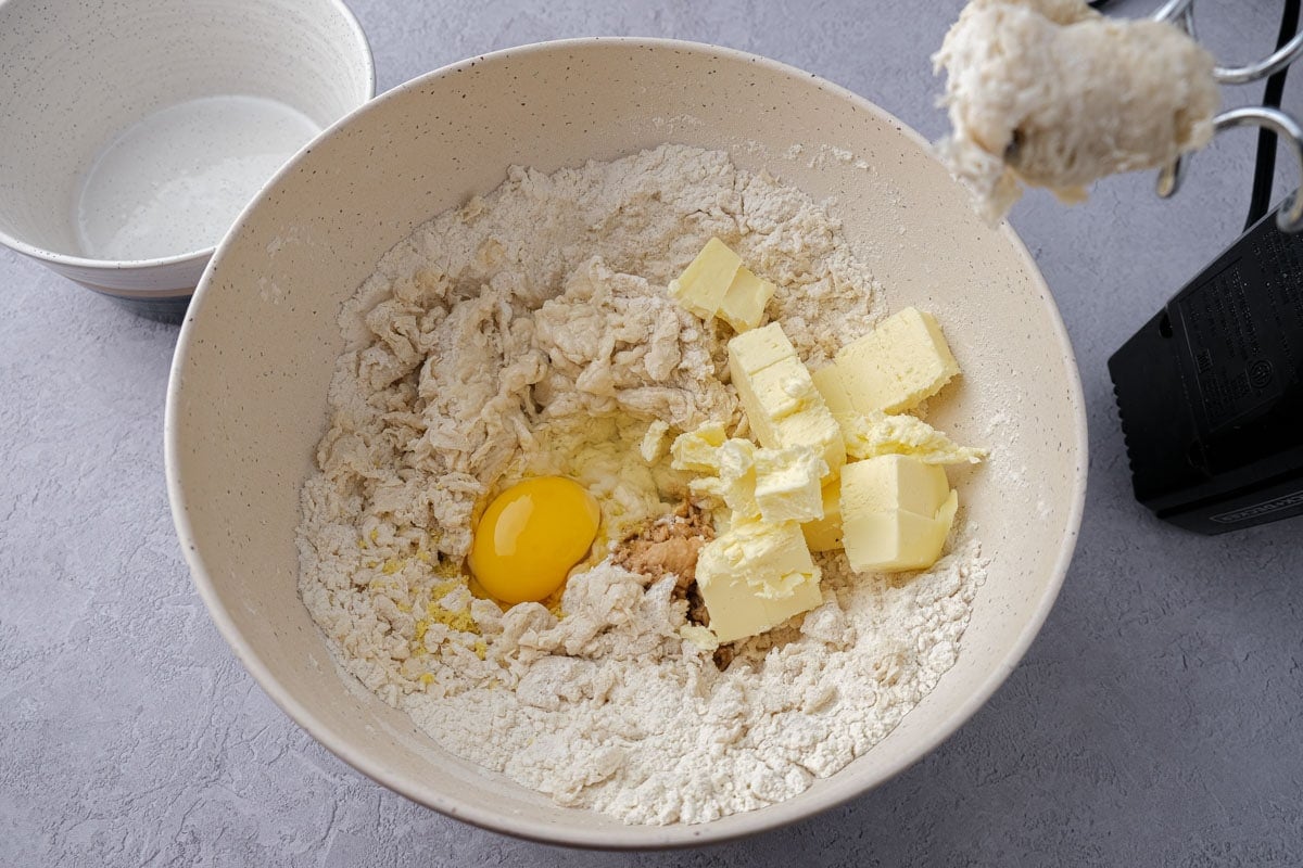 chunks of butter and egg yolk on top of dough in mixing bowl.