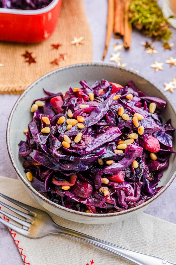 bowl of red cabbage with pine nuts with a silver fork in front in table.