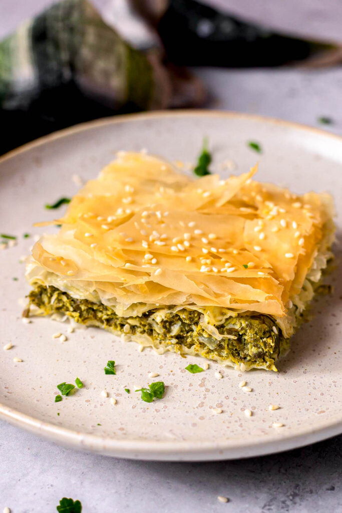 square slice of spanakopita on plate covered in sesame seeds.