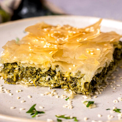 slice of spanakopita on plate covered in sesame seeds.