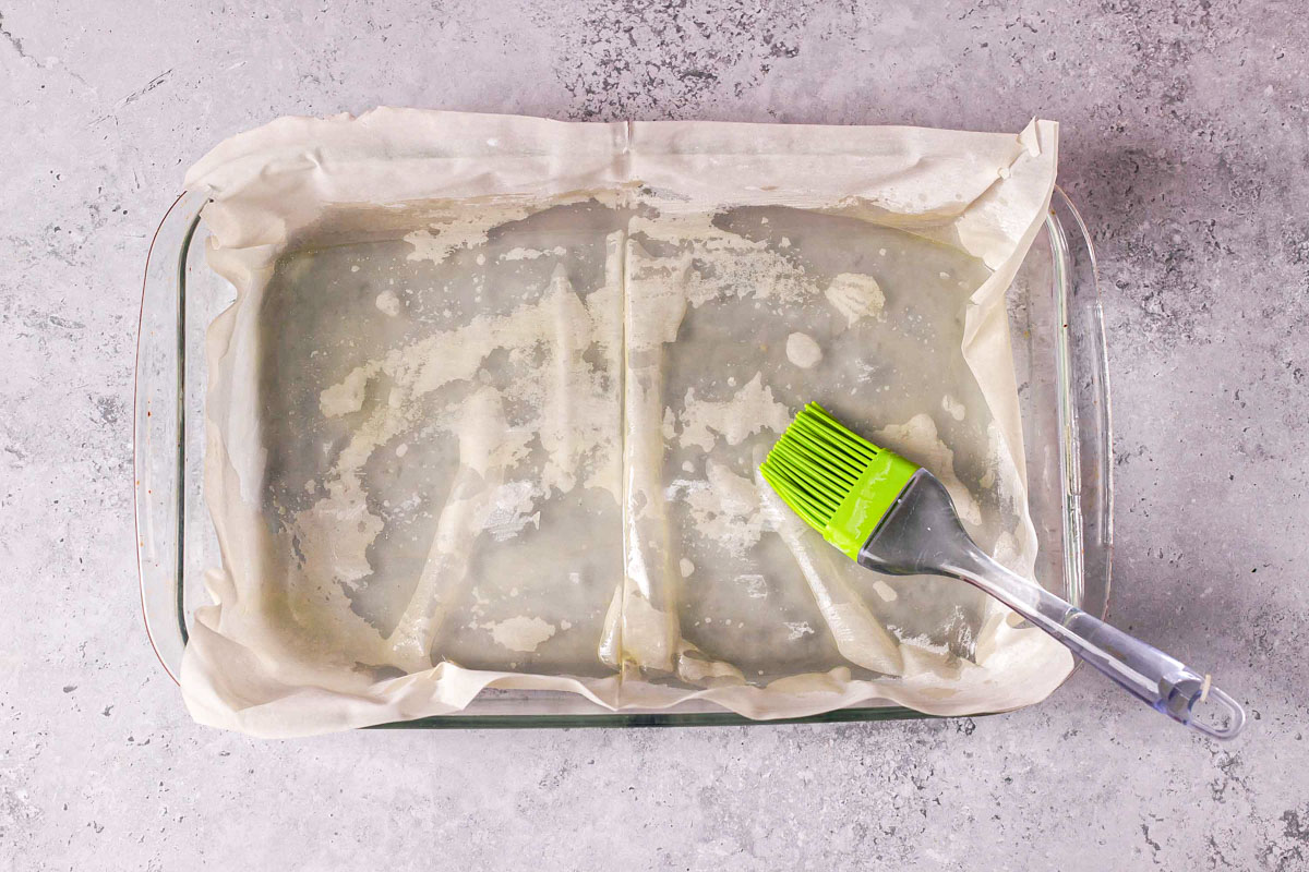 silicone brush brushing butter into phyllo sheets in baking pan.