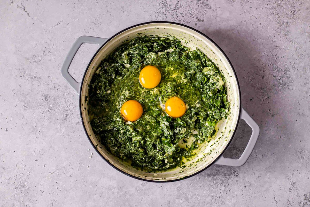 raw eggs cracked into large pot with spinach cheese mixture inside.