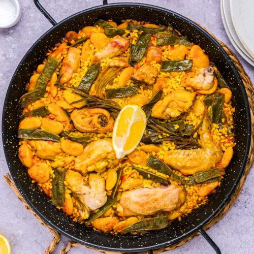 large black pan filled with paella valenciana ingredients cooked rice and rabbit.