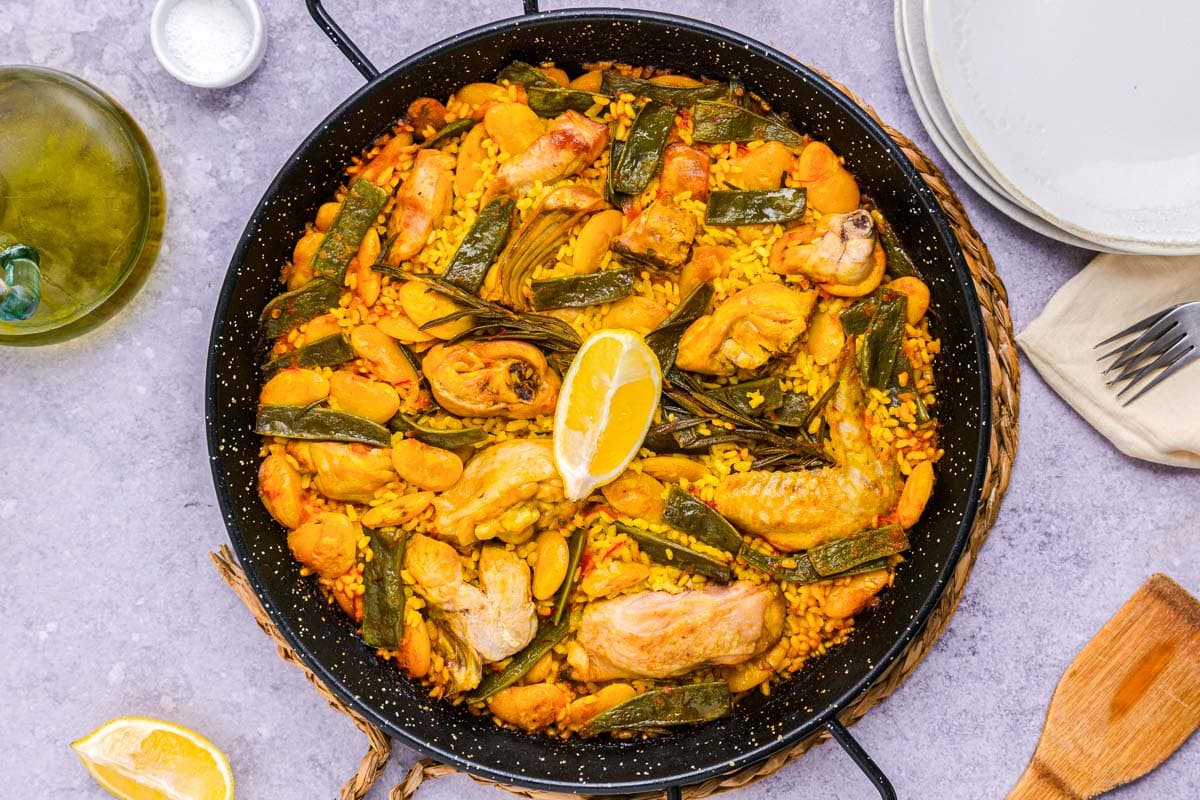large black pan filled with paella valenciana ingredients cooked rice and rabbit.