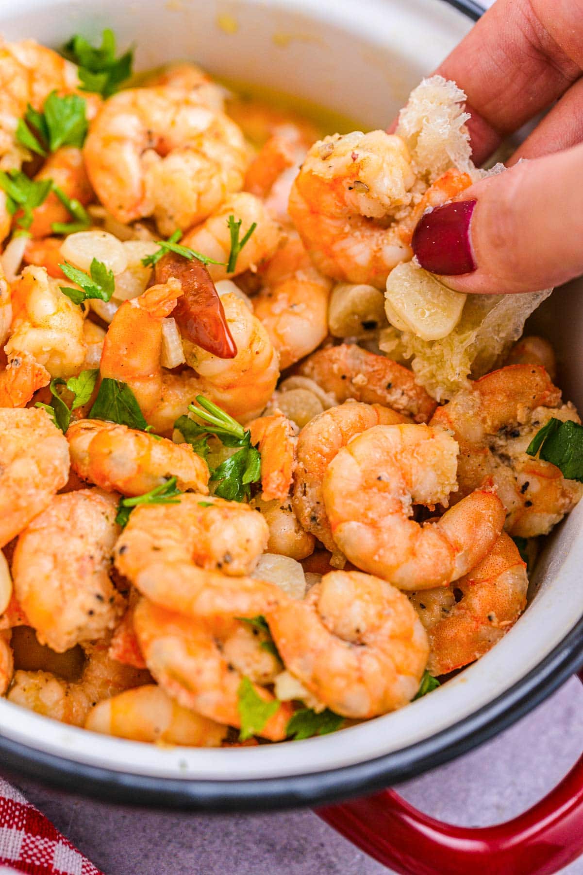 hand dipping bread into bowl of cooked garlic shrimp.
