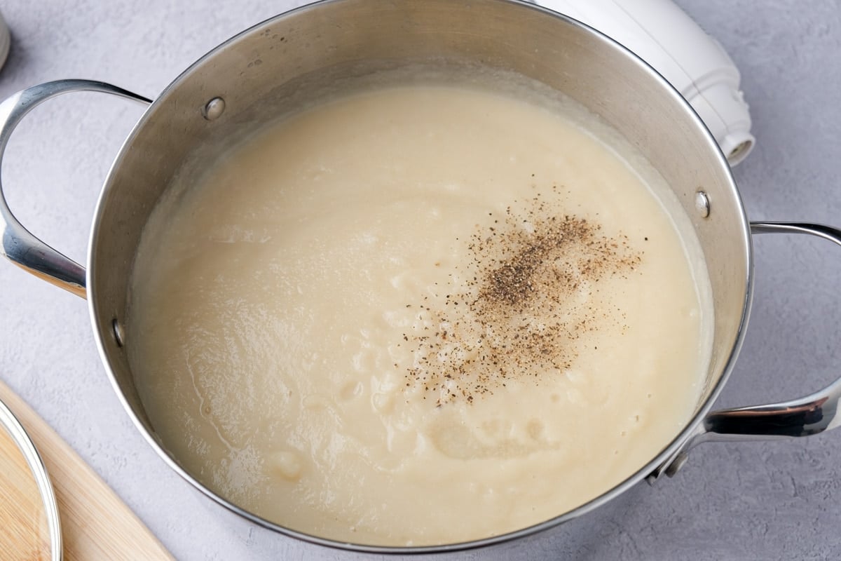 ground pepper sitting on top of celeriac soup in large silver pot.