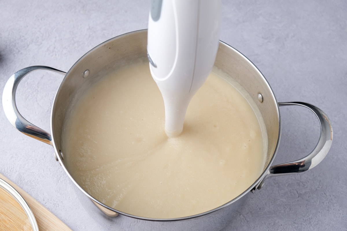 immersion blender sticking out of creamy soup in large silver pot.