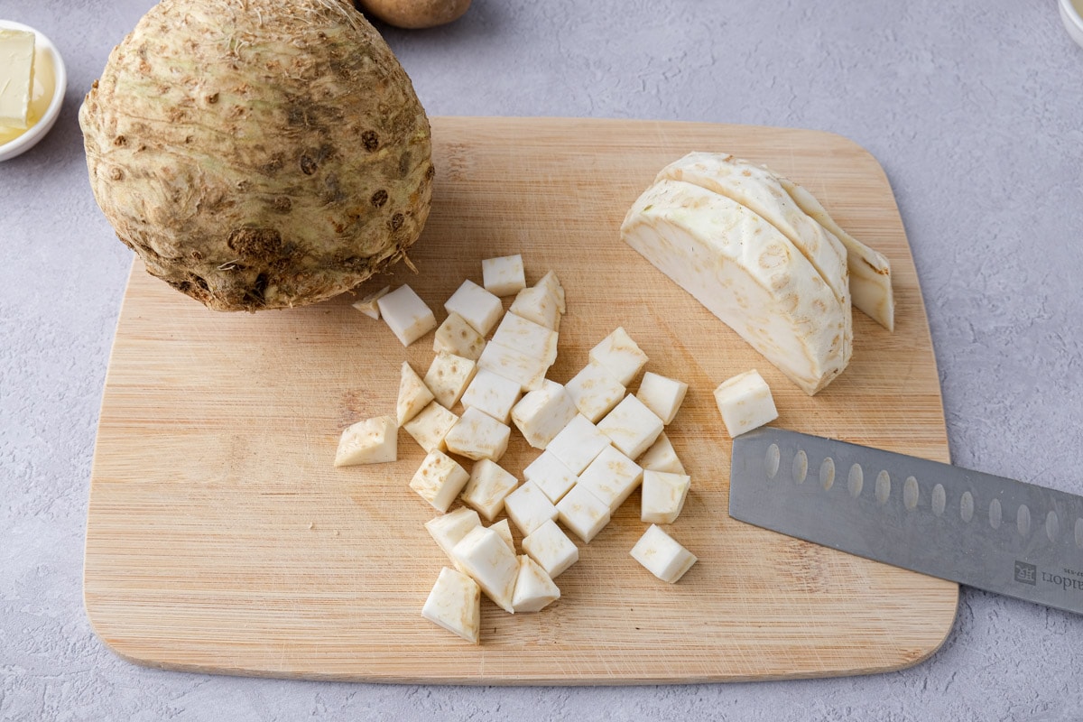 cubes of celeriac cut on wooden cutting board with knife laying beside.