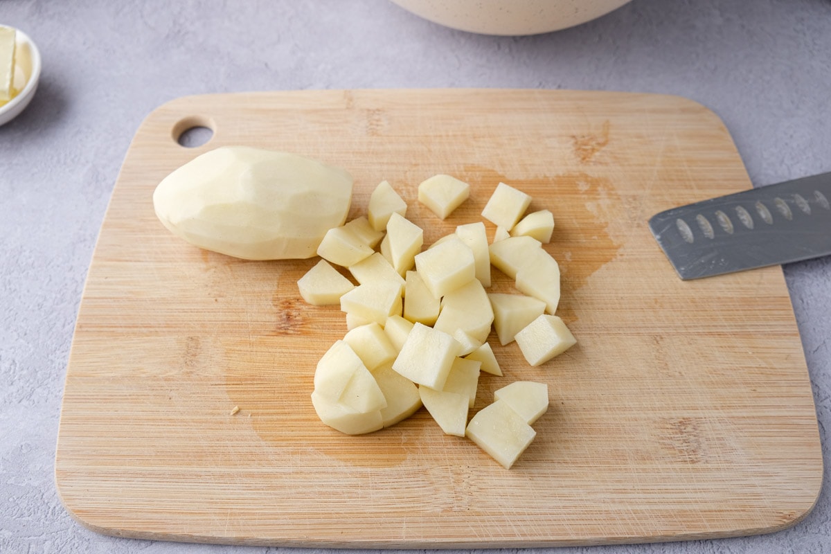 chunks of cut potato on wooden cutting board on counter with knife beside.