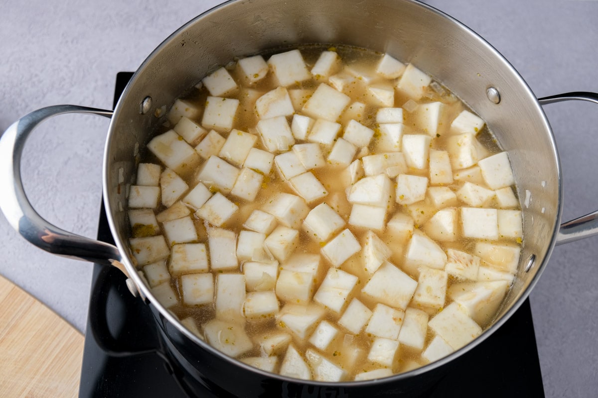 cubes of celeriac root and potatoes covered in broth in large silver pot.