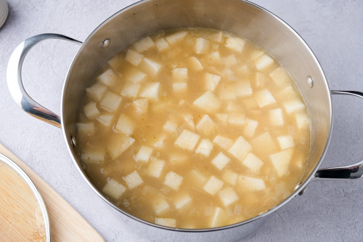 cloudy broth cooking celery root pieces in large silver pot on hot plate.