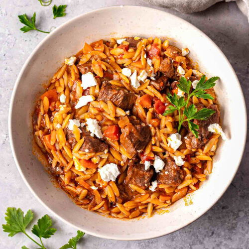 white bowl with greek beef and orzo stew in it sitting on counter.