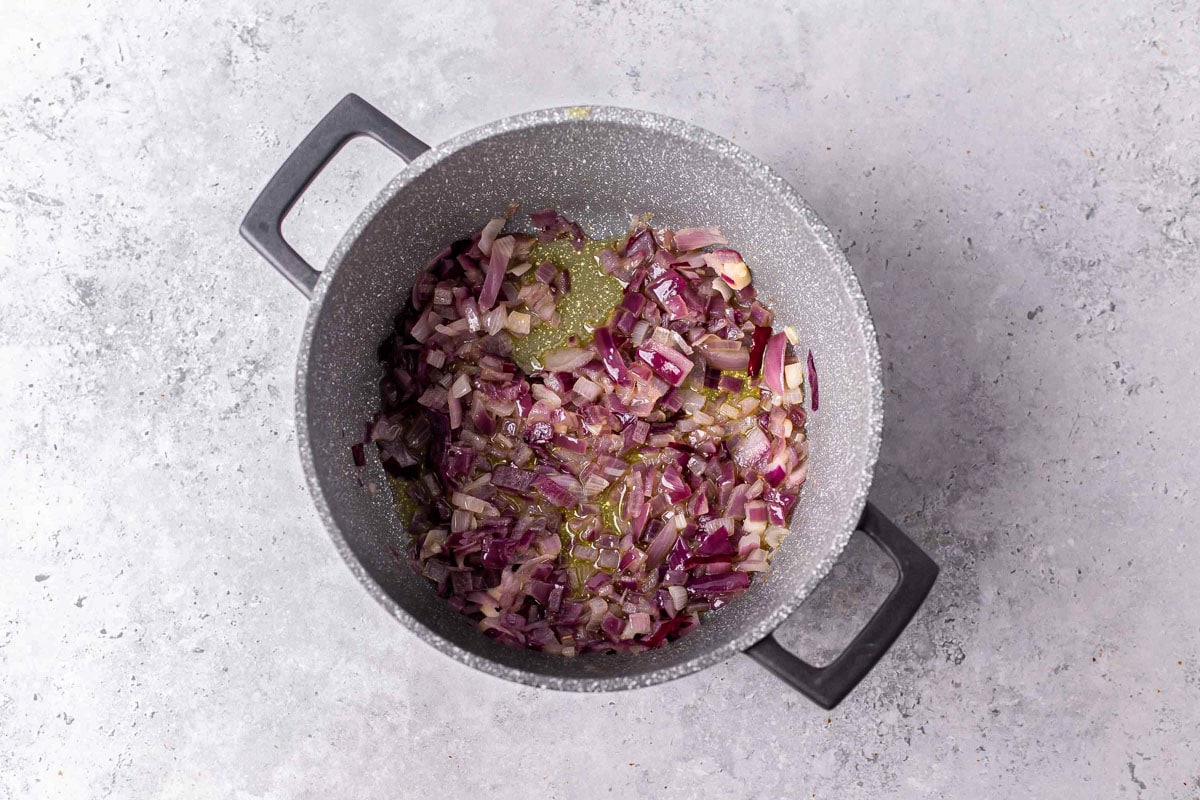 diced red onion frying in bottom of large pot sitting on counter.