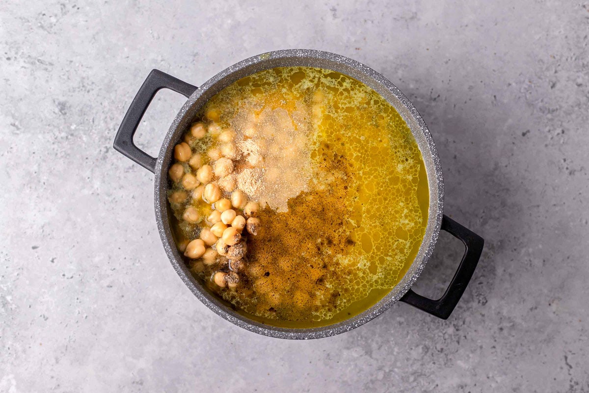 broth and chickpeas added to large soup pot with grey counter top around.