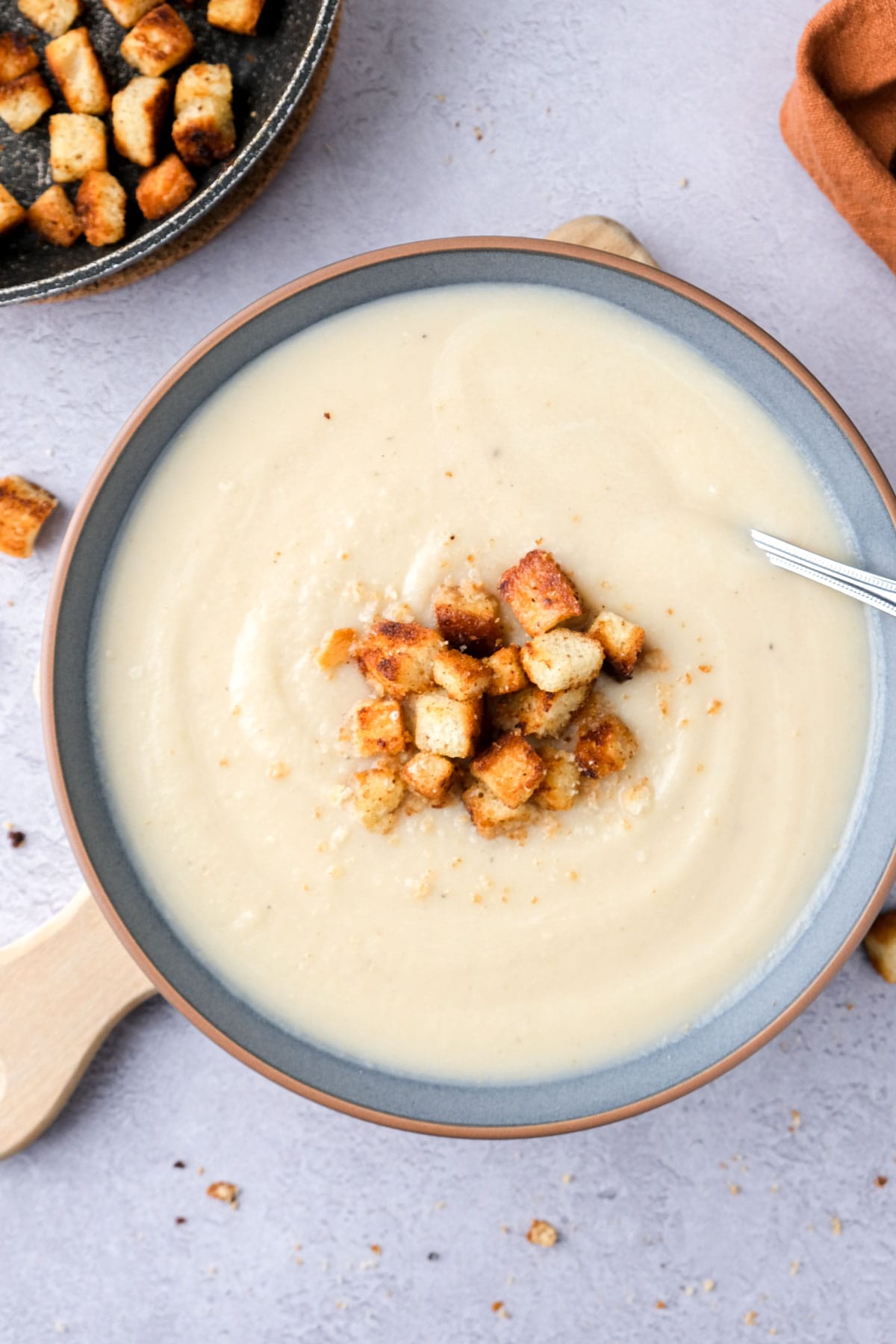 celeriac soup seen form top down in blue bowl with silver spoon and croutons on top.