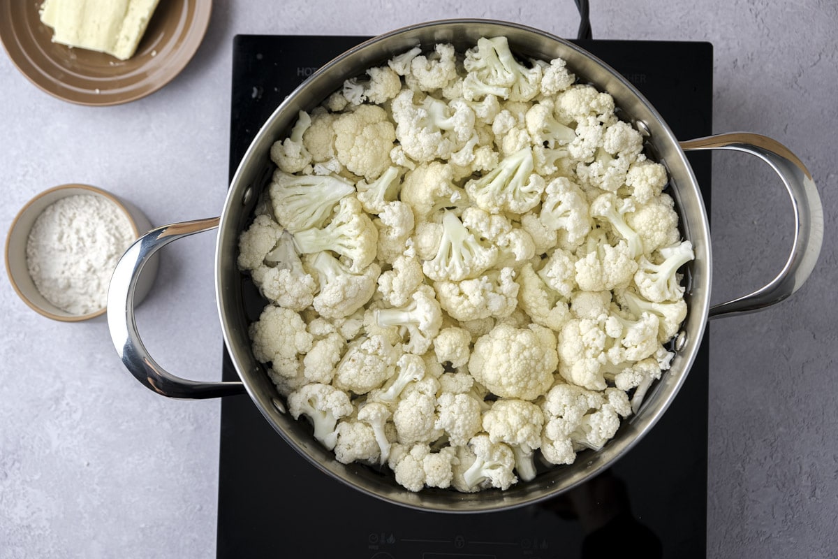cauliflower florets boiling in water in silver pot on hot plate.