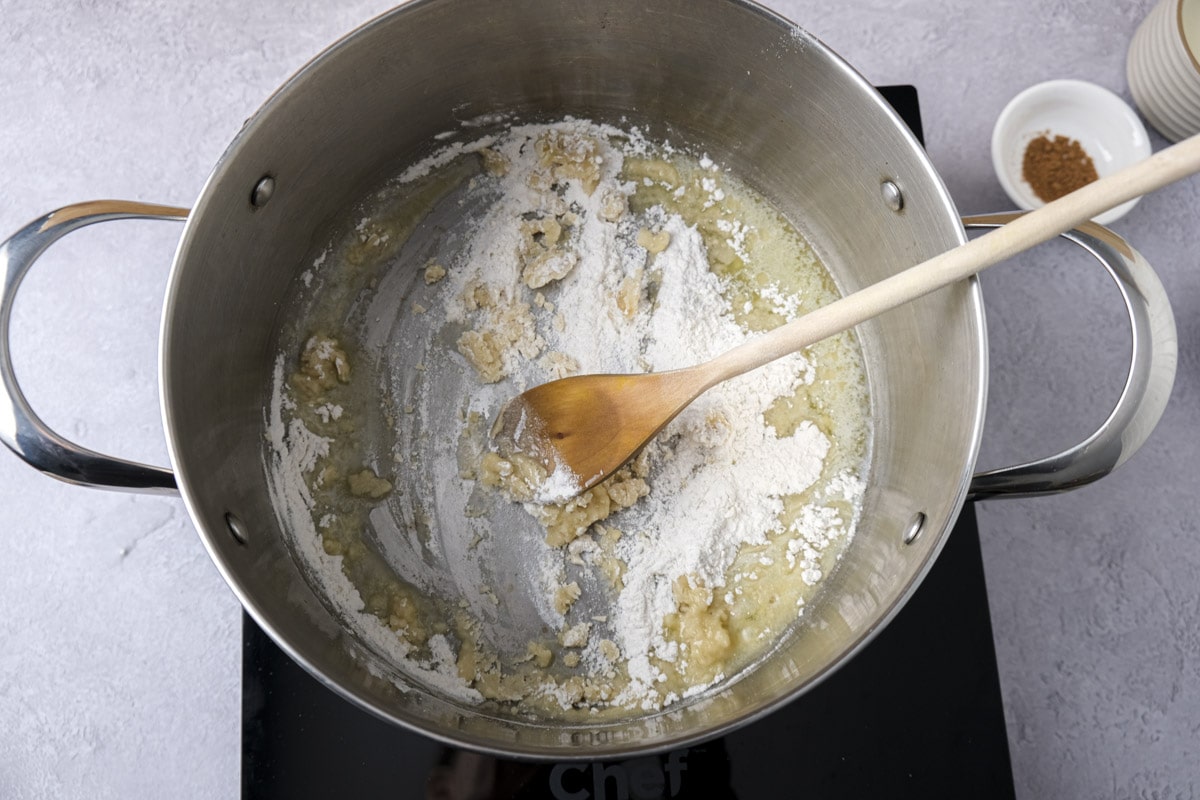 flour and butter being mixed in silver pot with wooden spoon inside.