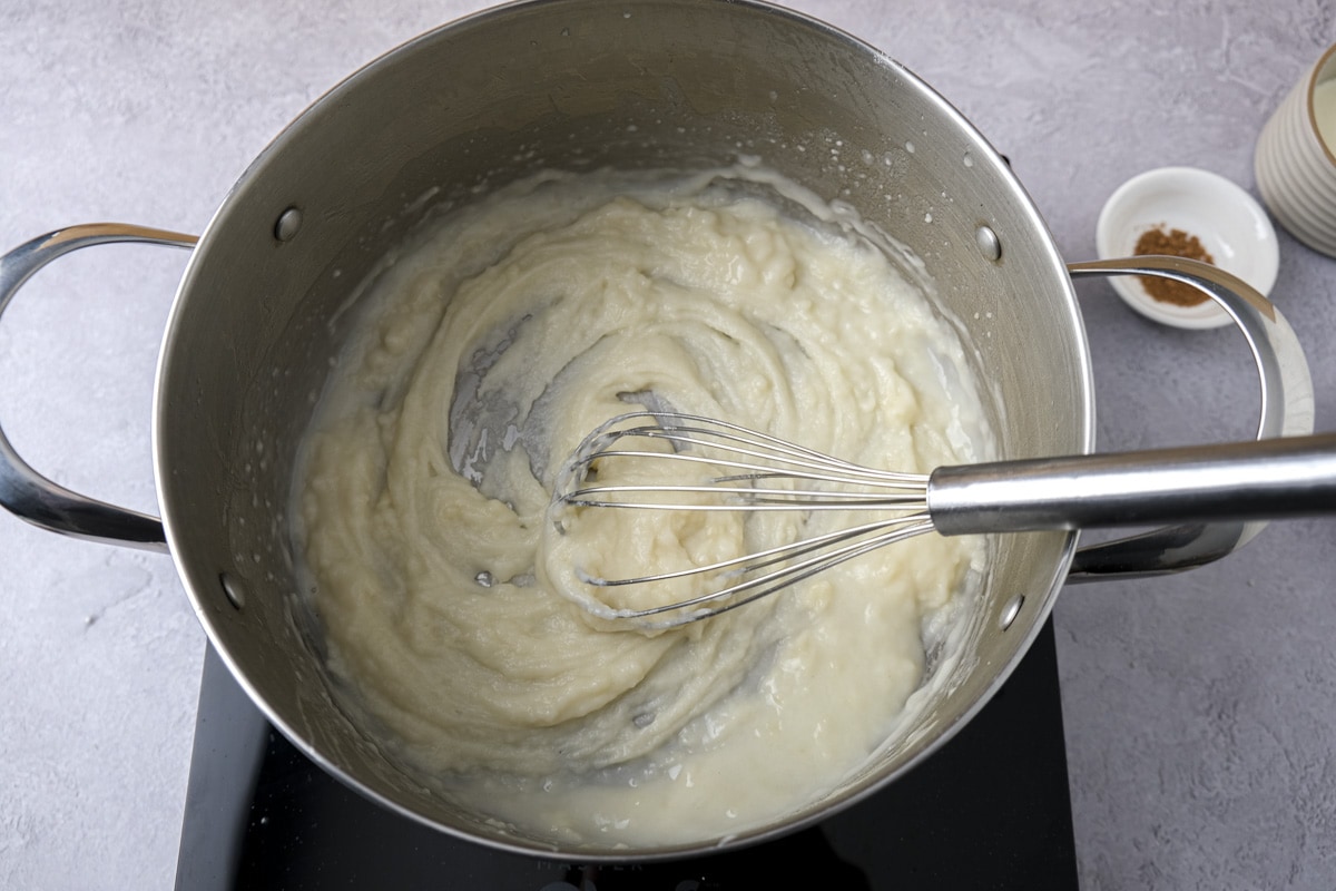 thickened roux in bottom of silver pot being mixed with silver whisk.