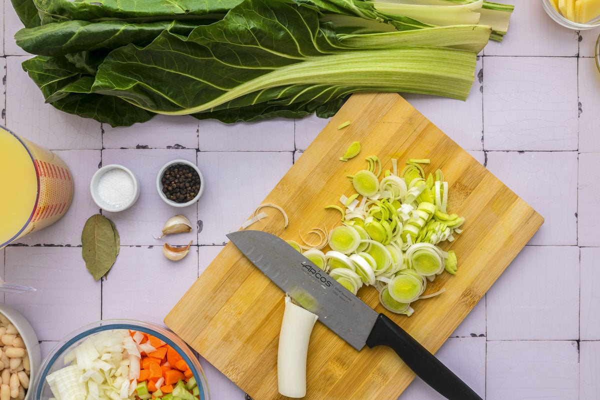 knife chopping leek on wooden cutting board with counter around.