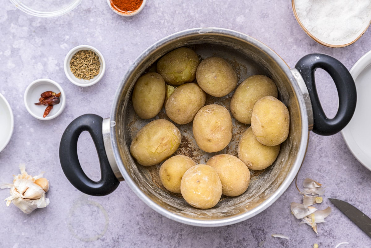wrinkled potatoes cooking in silver pot with spices around on counter.