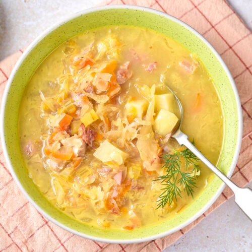 green bowl of sauerkraut soup with silver spoon sticking out resting on folded cloth.